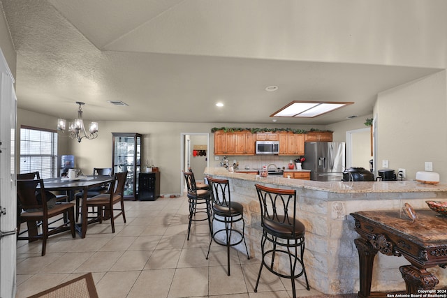 kitchen featuring a kitchen breakfast bar, light tile patterned floors, appliances with stainless steel finishes, kitchen peninsula, and a chandelier