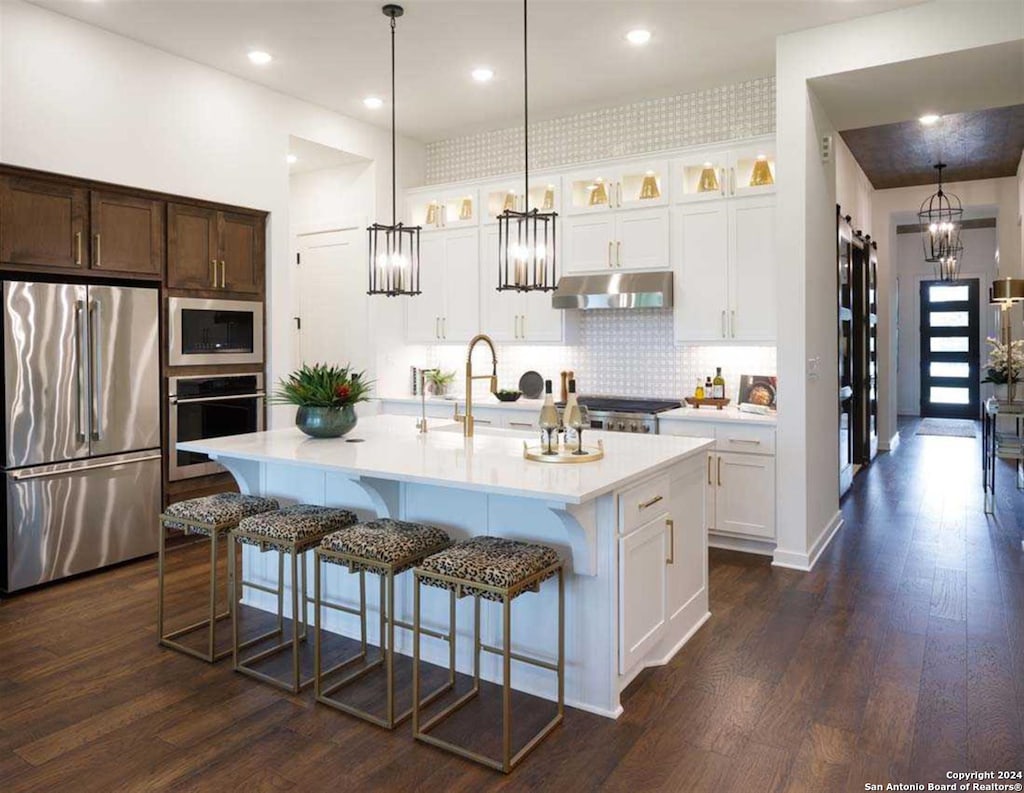 kitchen featuring a kitchen bar, white cabinetry, pendant lighting, stainless steel appliances, and a center island with sink