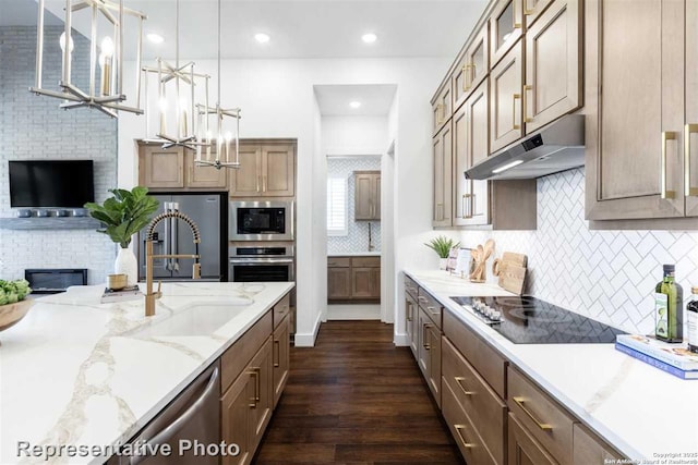 kitchen featuring appliances with stainless steel finishes, decorative light fixtures, light stone counters, a fireplace, and dark hardwood / wood-style floors