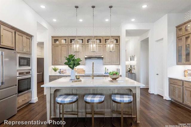 kitchen featuring black appliances, decorative light fixtures, dark wood-type flooring, a kitchen bar, and an island with sink