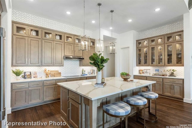 kitchen with light stone countertops, black electric stovetop, a kitchen island, pendant lighting, and a breakfast bar area