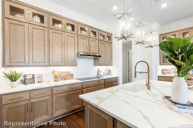 kitchen featuring decorative light fixtures, black electric stovetop, tasteful backsplash, sink, and light stone counters