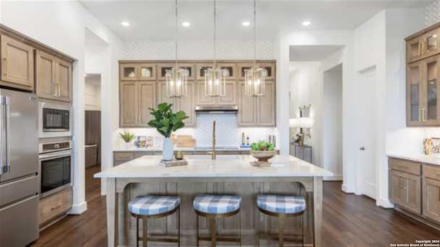 kitchen with a kitchen breakfast bar, a center island with sink, pendant lighting, and appliances with stainless steel finishes