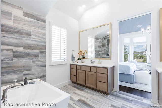 bathroom featuring tile walls, vanity, lofted ceiling, and a bathing tub