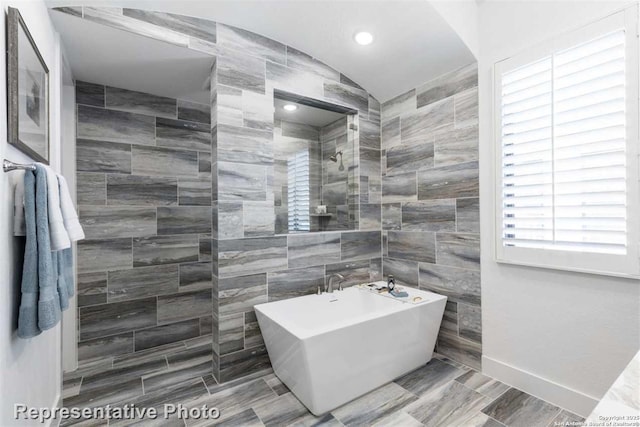 bathroom featuring vaulted ceiling, shower with separate bathtub, and tile walls