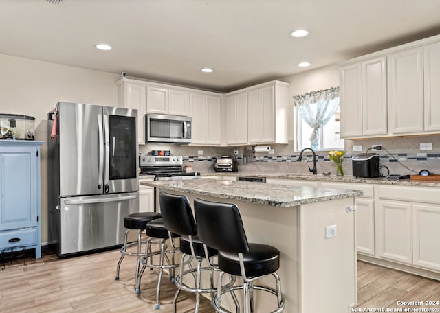 kitchen featuring stainless steel appliances, a center island, white cabinets, and light stone counters