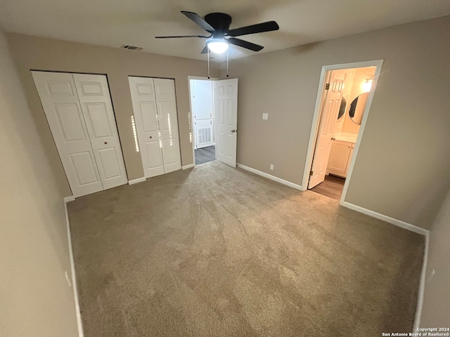 unfurnished bedroom featuring light carpet, two closets, ensuite bath, and ceiling fan