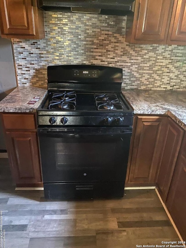 kitchen with dark stone counters, dark hardwood / wood-style floors, tasteful backsplash, gas stove, and extractor fan