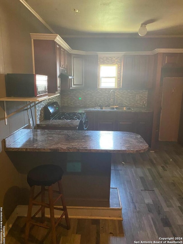 kitchen featuring sink, dark wood-type flooring, kitchen peninsula, decorative backsplash, and black range