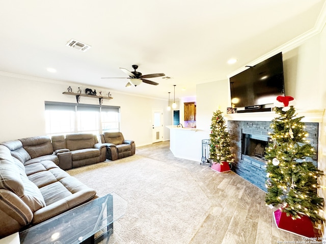 living room featuring ceiling fan, a stone fireplace, light wood-type flooring, and ornamental molding