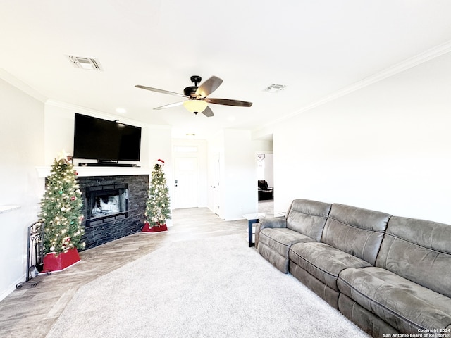 living room with light wood-type flooring, a stone fireplace, ceiling fan, and ornamental molding