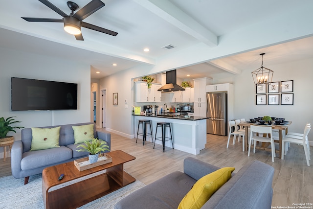 living room with ceiling fan with notable chandelier, light wood-type flooring, beamed ceiling, and sink