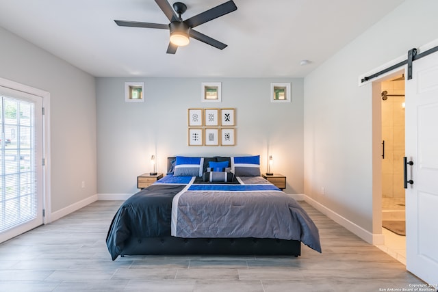 bedroom with a barn door, ceiling fan, light hardwood / wood-style flooring, and ensuite bath