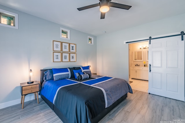 bedroom with ceiling fan, a barn door, ensuite bathroom, and light hardwood / wood-style flooring