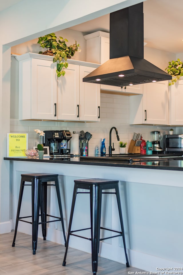 kitchen featuring white cabinets, a breakfast bar, backsplash, and island exhaust hood