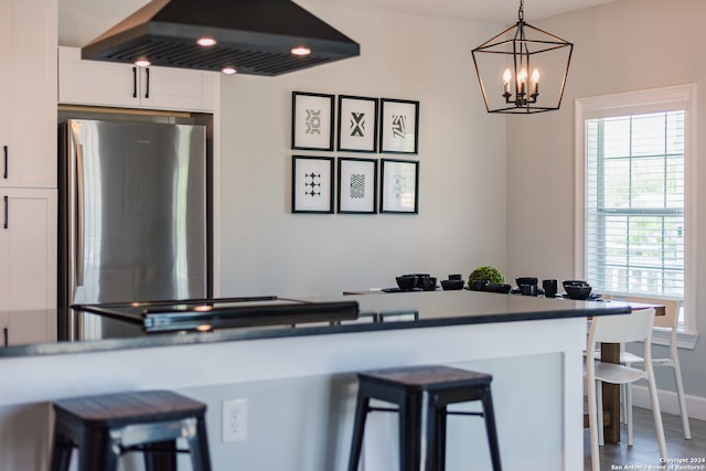 kitchen with white cabinets, ventilation hood, a breakfast bar area, and an inviting chandelier