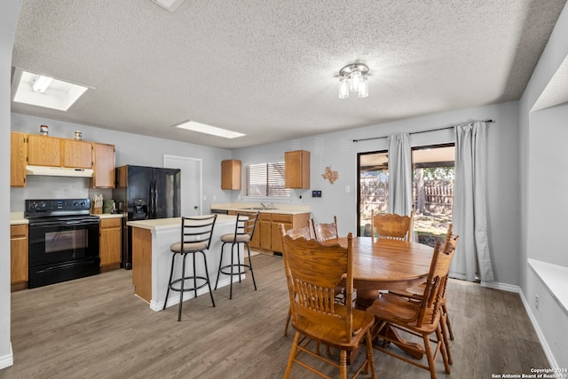 dining area featuring a textured ceiling, a skylight, sink, and light hardwood / wood-style flooring