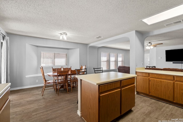 kitchen with ceiling fan, a kitchen island, light hardwood / wood-style floors, and a textured ceiling