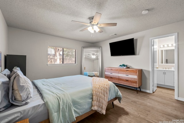 bedroom with ensuite bath, ceiling fan, light hardwood / wood-style flooring, and a textured ceiling