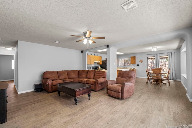 living room with ceiling fan, light hardwood / wood-style floors, and a textured ceiling