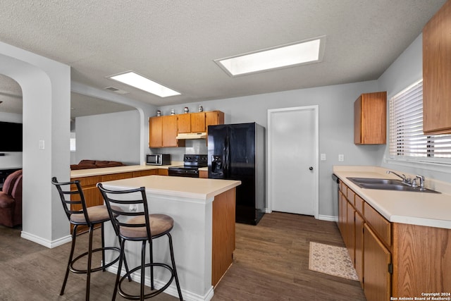 kitchen featuring a breakfast bar, black appliances, sink, dark hardwood / wood-style floors, and a textured ceiling