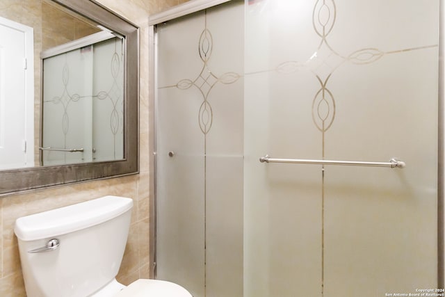 bathroom featuring a shower with shower door, tile walls, and toilet