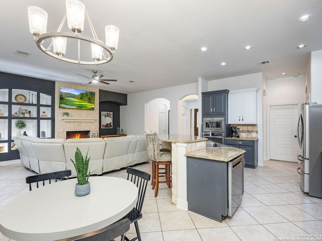 kitchen with decorative light fixtures, a center island with sink, light tile patterned floors, ceiling fan with notable chandelier, and appliances with stainless steel finishes