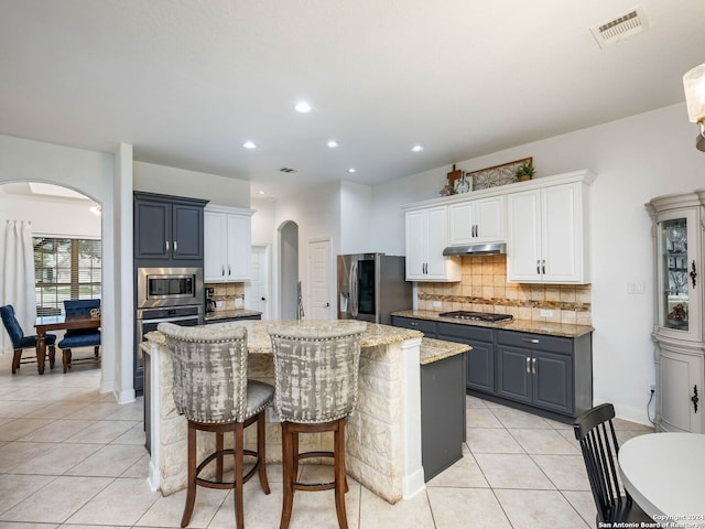 kitchen featuring decorative backsplash, appliances with stainless steel finishes, a kitchen island, light tile patterned floors, and white cabinetry