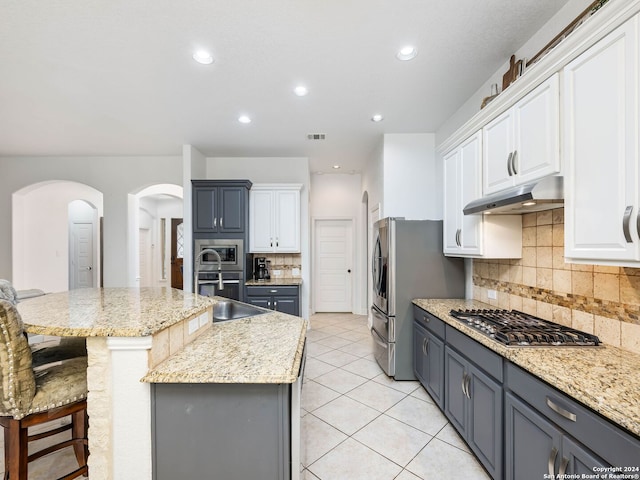 kitchen with white cabinetry, backsplash, a kitchen bar, a kitchen island with sink, and appliances with stainless steel finishes