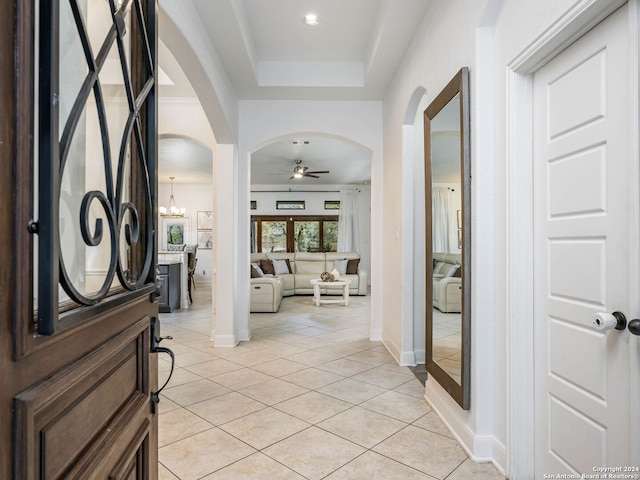 entryway featuring ceiling fan with notable chandelier, light tile patterned flooring, and a tray ceiling