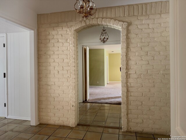 hall featuring tile patterned flooring, brick wall, and an inviting chandelier