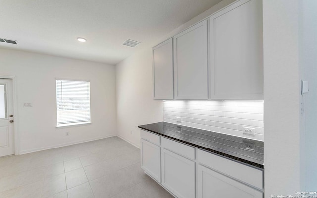 kitchen featuring light tile patterned floors, white cabinetry, dark stone counters, and tasteful backsplash