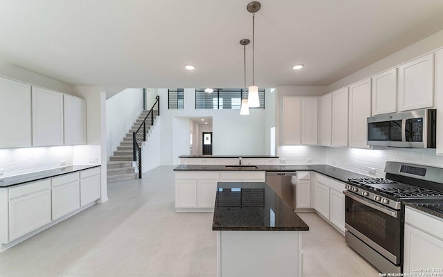 kitchen with white cabinetry, sink, stainless steel appliances, dark stone countertops, and pendant lighting