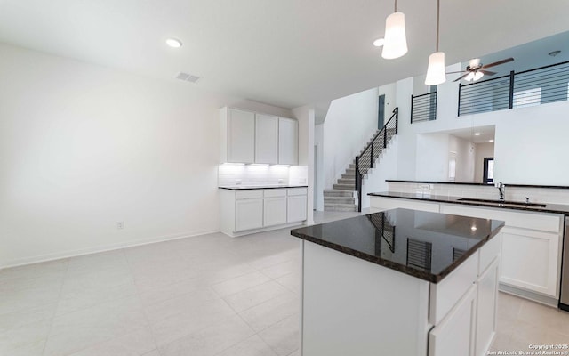 kitchen with ceiling fan, sink, a kitchen island, backsplash, and white cabinets