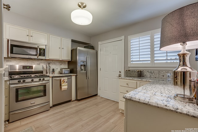 kitchen with appliances with stainless steel finishes, light stone counters, pendant lighting, light hardwood / wood-style flooring, and white cabinets