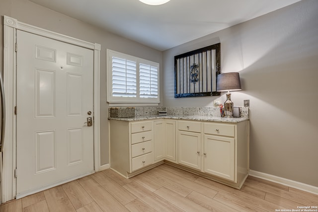 kitchen with cream cabinetry, light stone counters, and light wood-type flooring