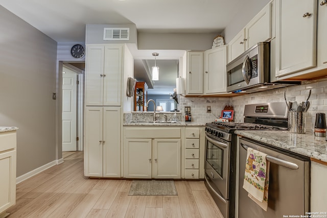 kitchen with light stone countertops, stainless steel appliances, sink, pendant lighting, and light hardwood / wood-style floors