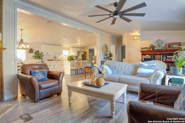 living room featuring ceiling fan with notable chandelier, ornamental molding, light hardwood / wood-style flooring, and vaulted ceiling