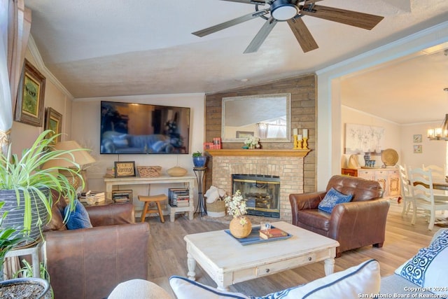 living room featuring ceiling fan with notable chandelier, a brick fireplace, vaulted ceiling, light wood-type flooring, and ornamental molding