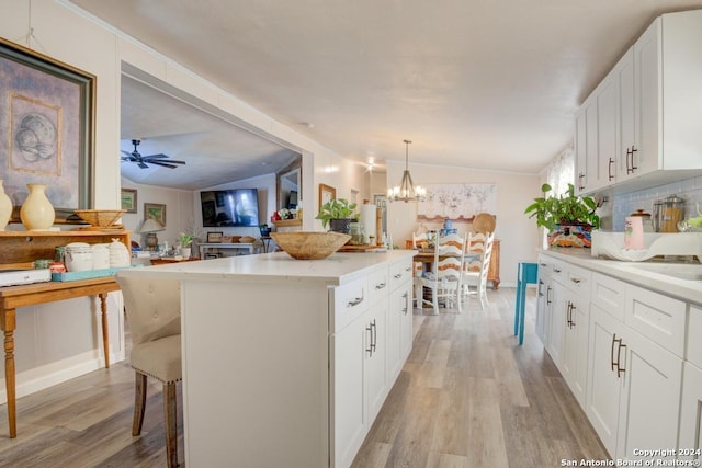 kitchen with a kitchen island, decorative light fixtures, light hardwood / wood-style floors, white cabinetry, and lofted ceiling