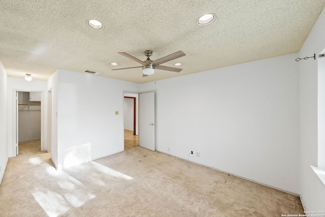 unfurnished bedroom with light carpet, a textured ceiling, ceiling fan, and a walk in closet