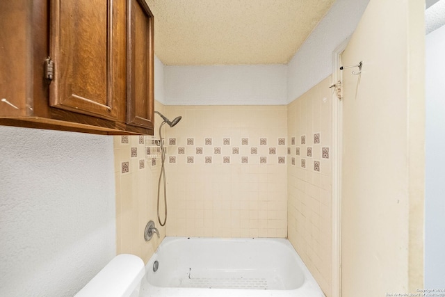 bathroom featuring a textured ceiling, toilet, and tiled shower / bath