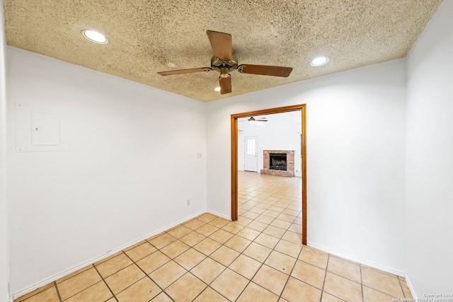 tiled empty room with ceiling fan, a textured ceiling, and a brick fireplace