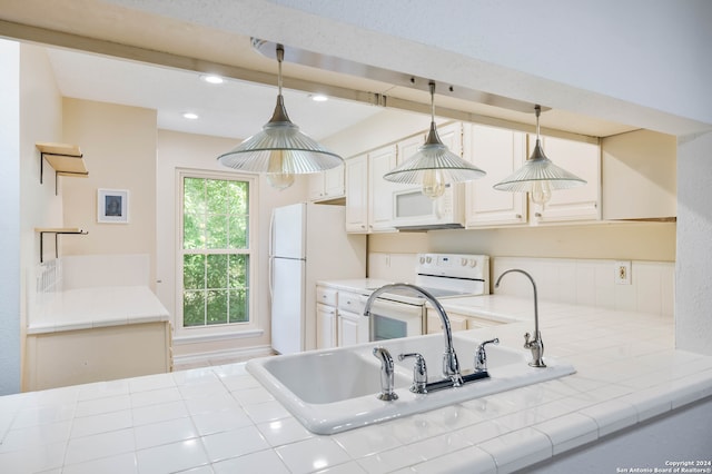 kitchen with hanging light fixtures, white appliances, white cabinetry, and tile counters