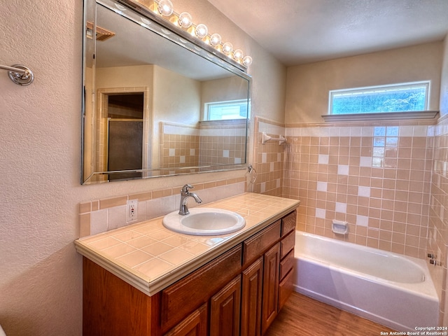 bathroom with hardwood / wood-style flooring, vanity, decorative backsplash, and tiled shower / bath combo