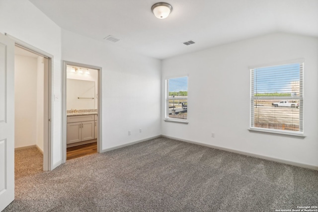 unfurnished bedroom featuring multiple windows, ensuite bathroom, carpet floors, and vaulted ceiling