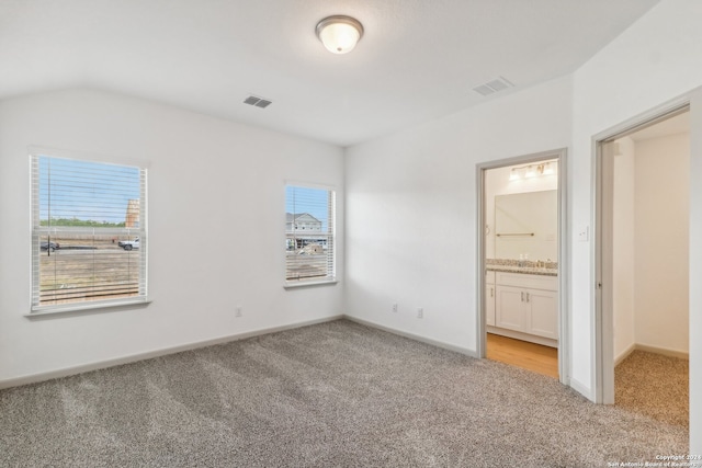 unfurnished bedroom with connected bathroom, multiple windows, light colored carpet, and lofted ceiling