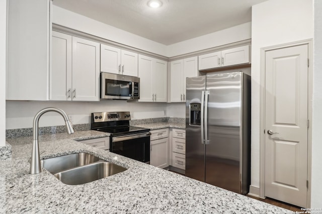 kitchen with light stone countertops, stainless steel appliances, white cabinets, and sink