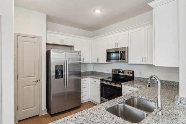 kitchen with hardwood / wood-style floors, sink, light stone countertops, appliances with stainless steel finishes, and white cabinetry