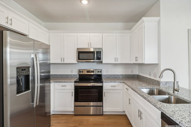 kitchen with white cabinets, sink, light wood-type flooring, appliances with stainless steel finishes, and light stone counters